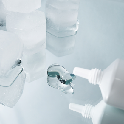 Close-up of a white tube with a dropper dispensing clear liquid onto a white surface.