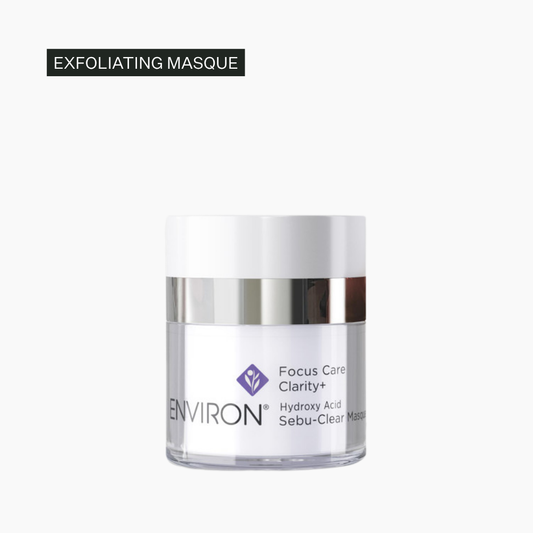 A clear cosmetic jar with a white lid and silver band, labeled ENVIRON Focus Care Clarity+ Hydroxy Acid Sebu-Clear Masque, on a light gray background with a black text label reading 'EXFOLIATING MASQUE' at the top left.