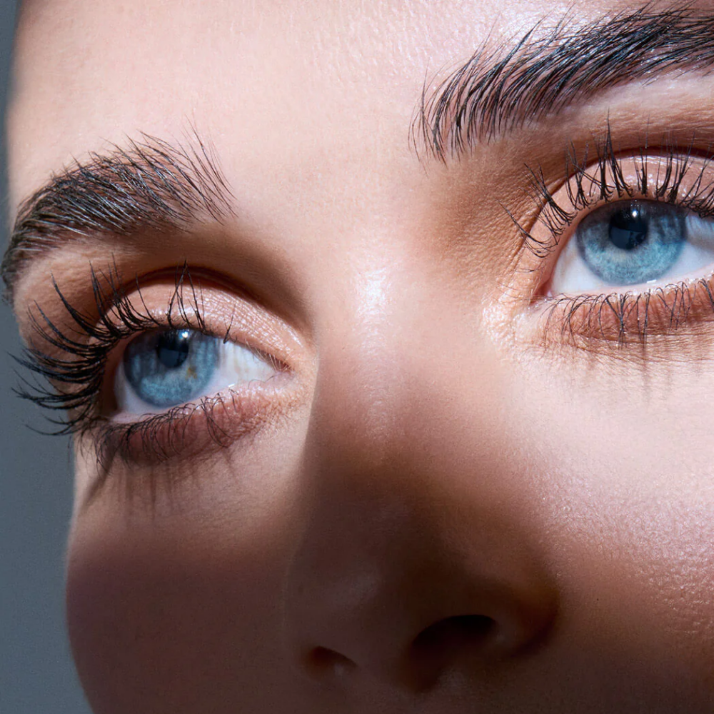 Extreme close-up of a person's eyes wearing long, dark, curled eyelashes and defined eyebrows, with warm-toned eyeshadow and smooth skin.
