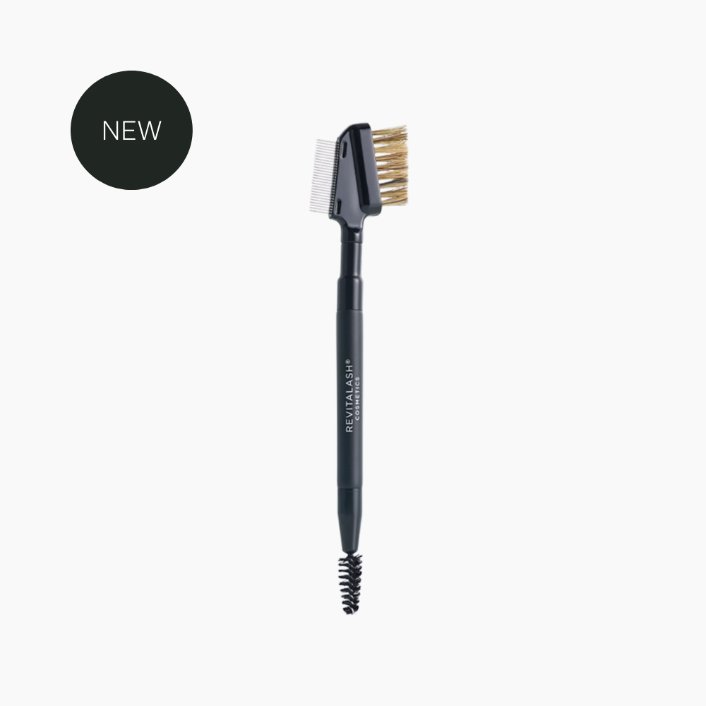 A dual-ended brow and eye brush with a black handle, white and gold bristles, and a spoolie end, shown on a light gray background with a black circular 'NEW' badge in the top left.