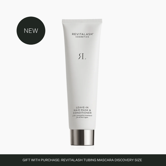 A white squeeze tube of Revitalash Cosmetics Leave-In Hair Mask & Conditioner with a metallic silver cap, shown on a light gray background with a black circular 'NEW' badge and a dark gray banner at the bottom.