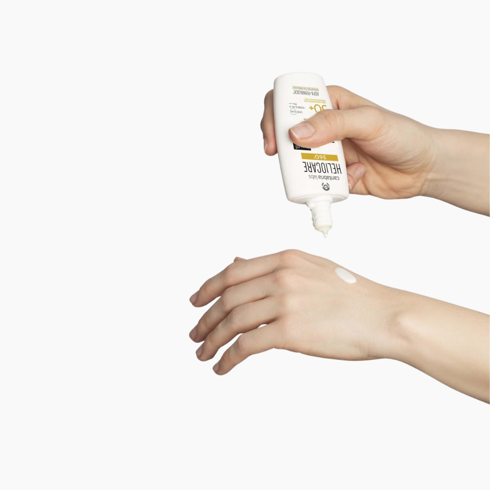 A hand holds a white sunscreen bottle above another hand, with a small dollop of cream being squeezed onto the back of the hand against a plain white background.